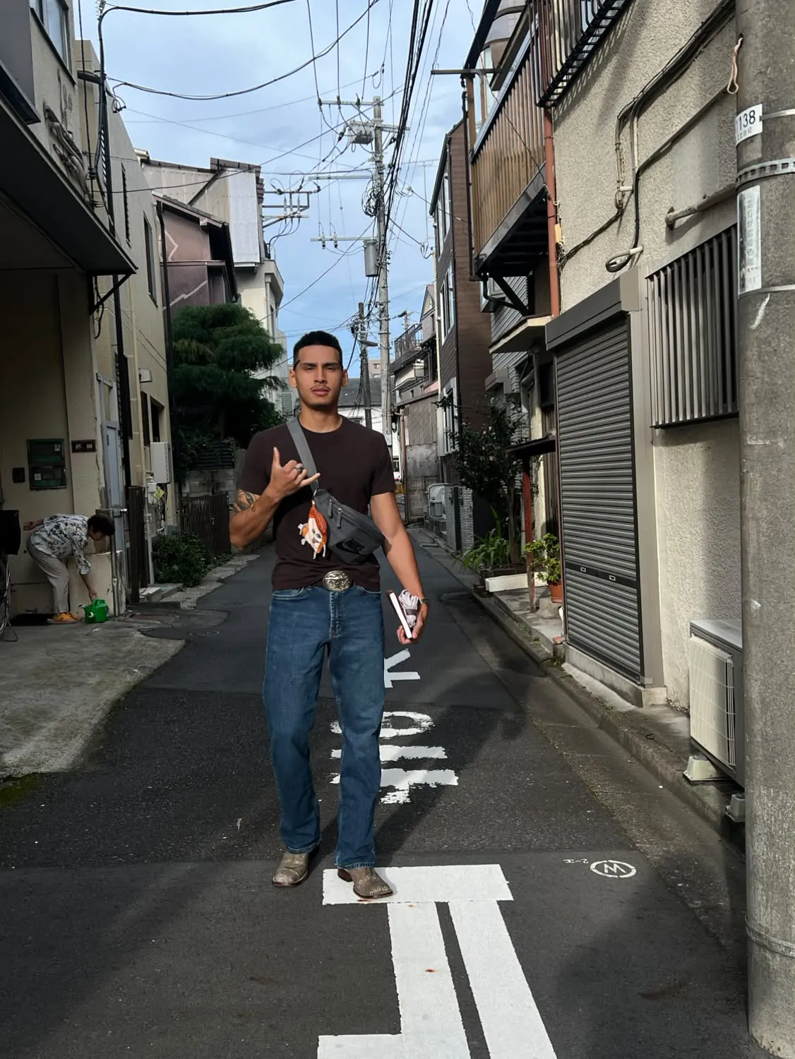 Portrait of the artist standing in a narrow residential street, wearing a dark tee, denim and boots
